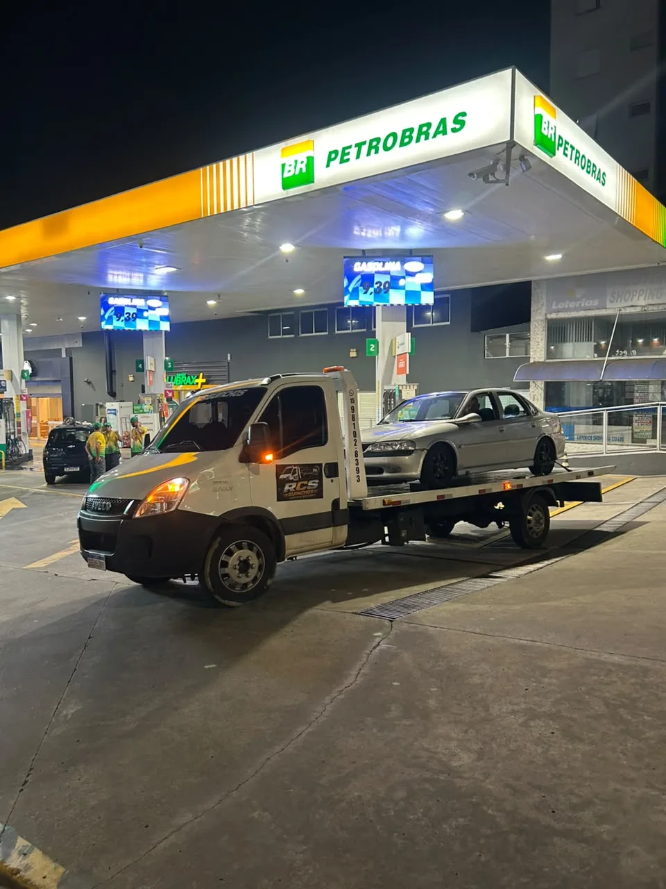 Guincho plataforma da RCS com carro carregado em um posto de combustível à noite